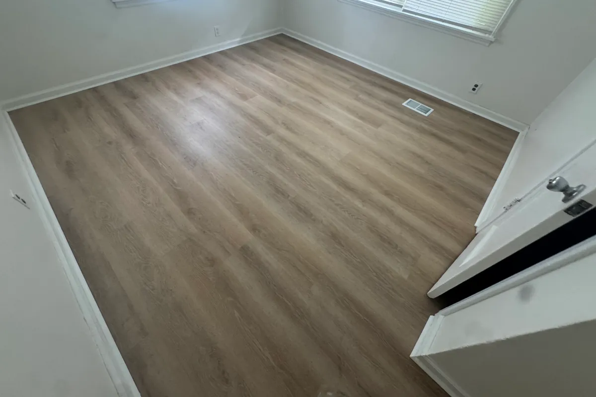 Empty bedroom with newly installed luxury vinyl plank flooring running wall to wall, baseboard and quarter round finished at the edges.