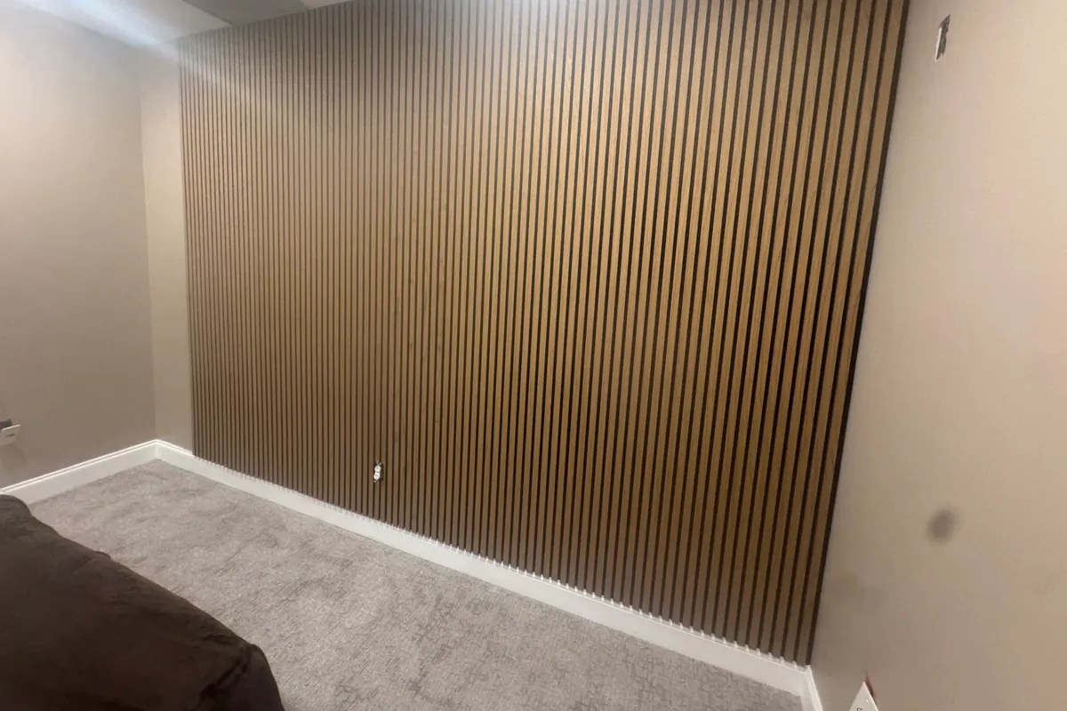 Finished room with a floor-to-ceiling vertical wood slat accent wall in a dark stain, running the full width behind a light wall and trim.