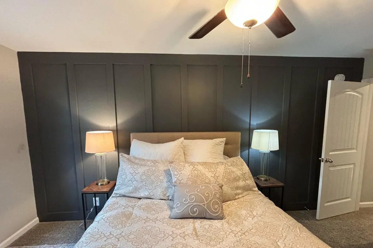 Bedroom accent wall built in board and batten and painted a deep charcoal, running floor to ceiling behind the bed with light gray walls and white trim on either side.