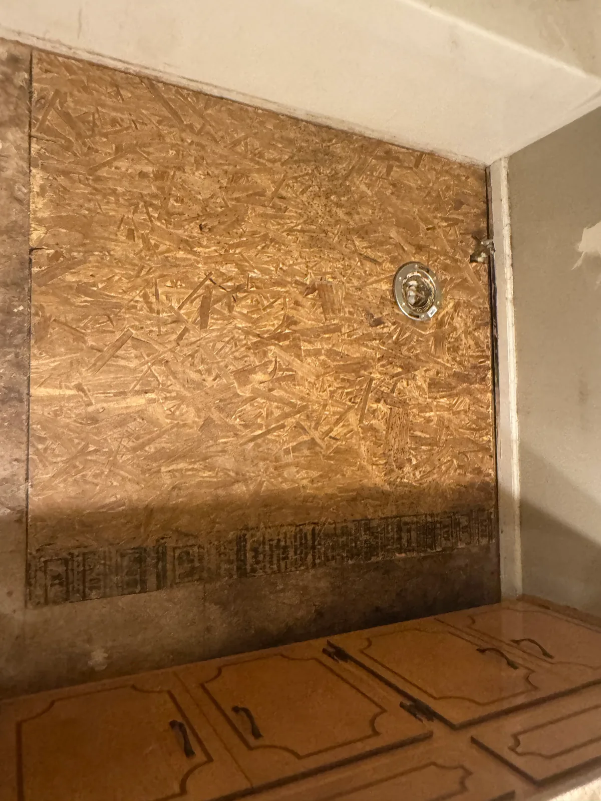 The same wall closed back up with new OSB sheathing cut tight around the shower valve escutcheon, ready for the surround to go back on, with the cabinets below untouched.
