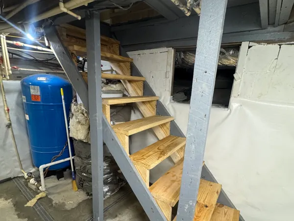 New pressure treated basement stair stringers with treads part way installed, framing and the wall opening visible behind.