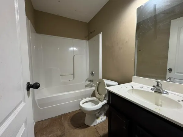 The same bathroom cleared out, with the shelf unit, the toiletries and the curtain gone and nothing left on the vanity or the tub surround.