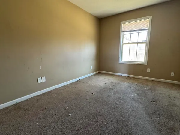 A bedroom in the same rental emptied down to bare carpet and walls, nothing left in the room and the window uncovered.