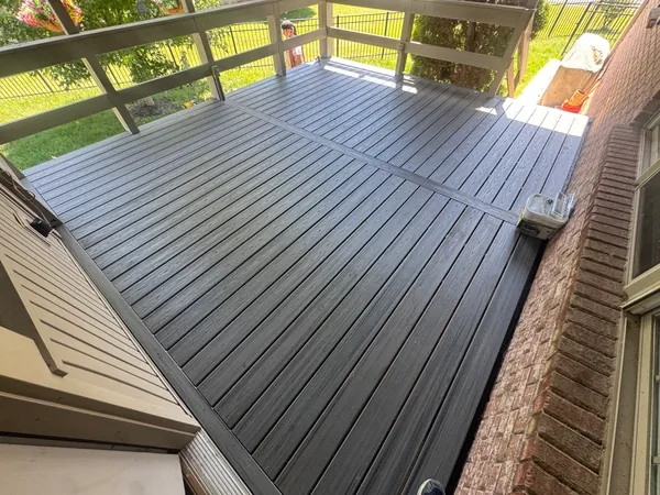 New gray composite deck boards laid tight across a screened porch, with the porch framing and screen posts standing above the deck surface.
