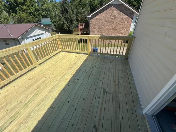 Newly built raised deck in bare green pressure treated lumber, boards run straight and tight with a full picket rail around two sides, looking out over neighbouring roofs.