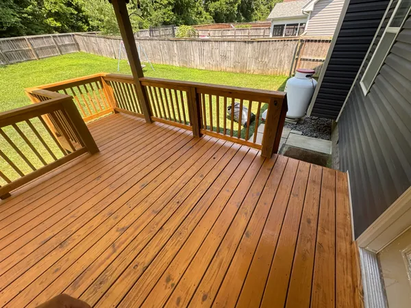 Wood deck looking across freshly cleaned and sealed boards in a warm honey tone, still wet-looking, with a matching rail and a privacy-fenced back yard beyond it.