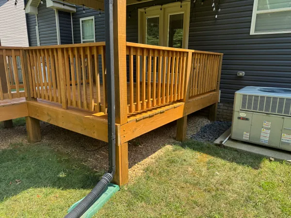The same deck seen from the yard, raised on posts against dark blue siding, with the rail, skirt board and posts all carrying the same fresh honey-toned sealer.