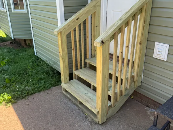 New pressure treated deck steps and railing built at a side entry door, treads cut square and the handrail fastened solid.