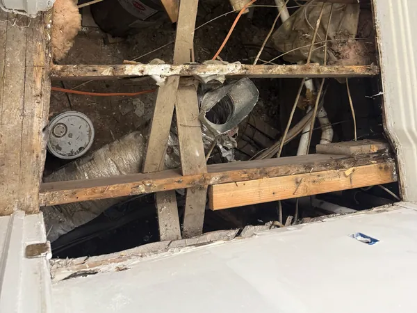 Ceiling opened up to the bare joists with older drain lines exposed above, drywall cut back cleanly around the work area.