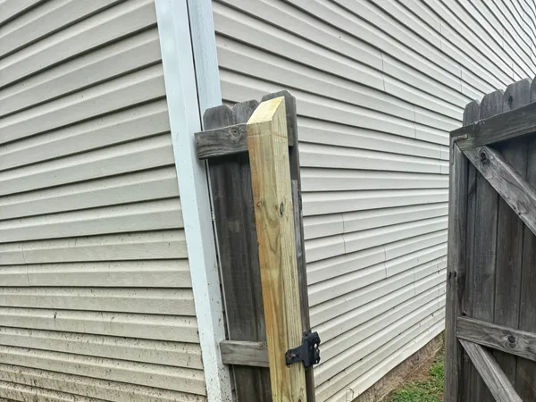 Freshly set pressure treated fence post standing next to the weathered gray boards of the existing older fence it is replacing.