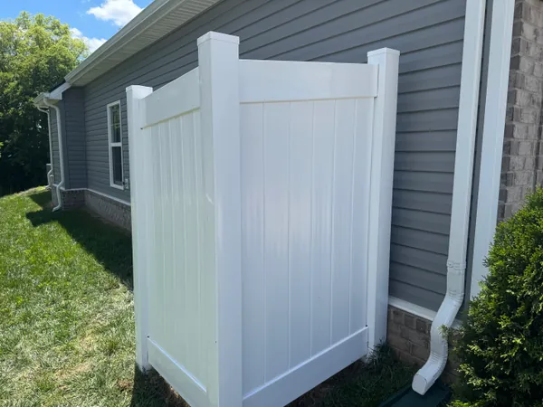 New white vinyl privacy fence section standing straight against a gray sided house, panels flush and posts plumb.