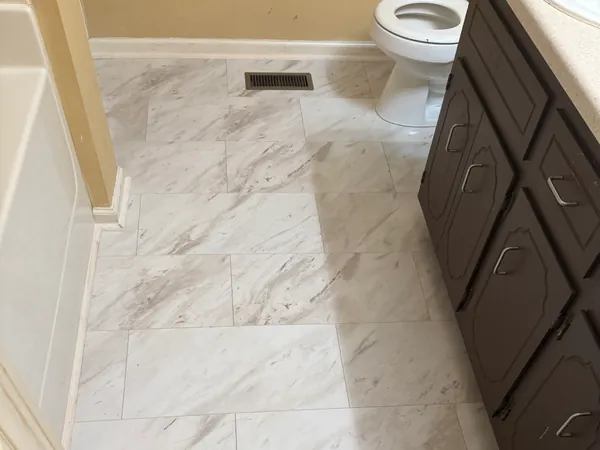 Bathroom with a new marble-look tile floor laid up to the vanity and tub, grout lines clean and even.