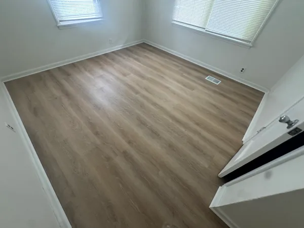 Empty bedroom with newly installed luxury vinyl plank flooring running wall to wall, baseboard and quarter round finished at the edges.