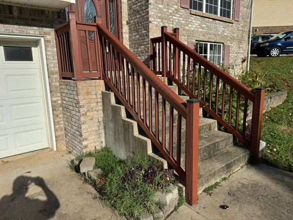 New wood handrail and balustrade stained dark red, built down both sides of a set of concrete front steps at a brick house and matching the rail on the porch landing above.
