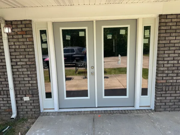 New white French patio doors installed in a brick exterior wall, trimmed out and closed square in the opening.