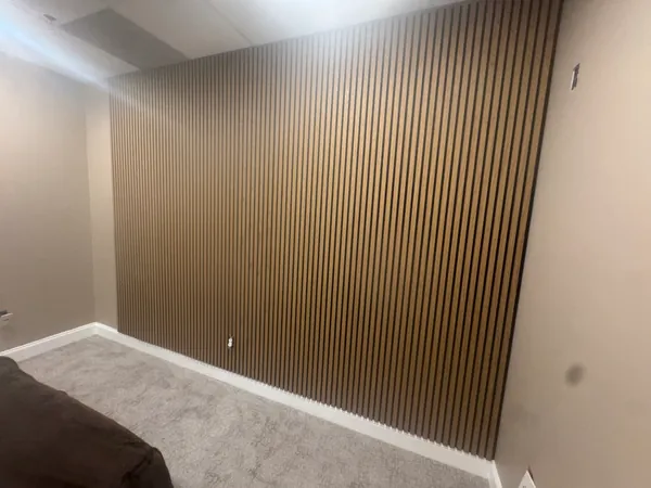 Finished room with a floor-to-ceiling vertical wood slat accent wall in a dark stain, running the full width behind a light wall and trim.