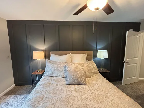 Bedroom accent wall built in board and batten and painted a deep charcoal, running floor to ceiling behind the bed with light gray walls and white trim on either side.
