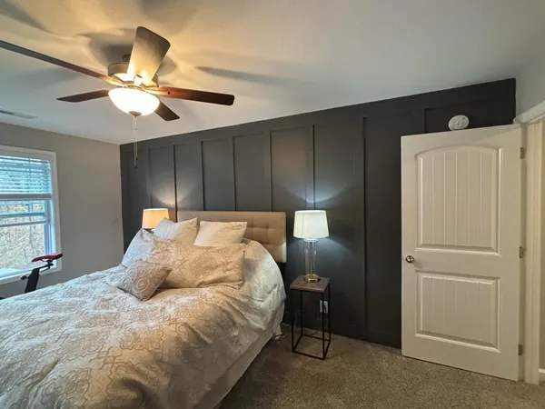 Wider view of the same bedroom showing the charcoal board and batten wall carried the full width to the door casing, with the light gray adjoining wall and the white ceiling cut in above it.