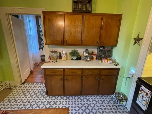 Kitchen cabinet run in its original orange-toned wood stain, upper and lower boxes with the old ring pulls, against a lime green wall.