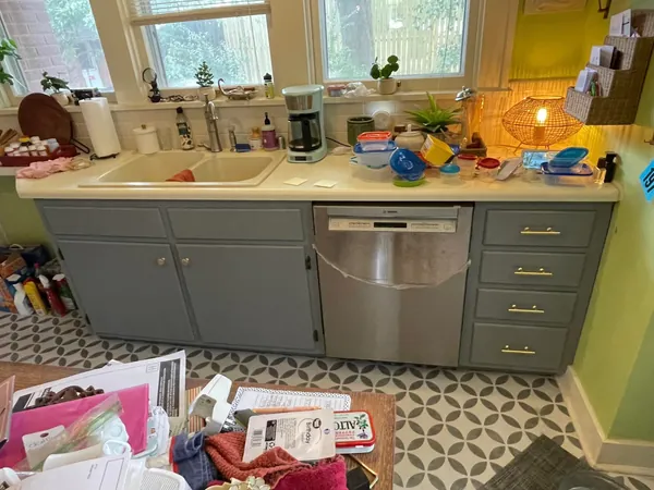 The same sink run repainted slate gray-blue with new brass bar pulls, cut in clean where the cabinet boxes meet the counter and the dishwasher panel beside them.