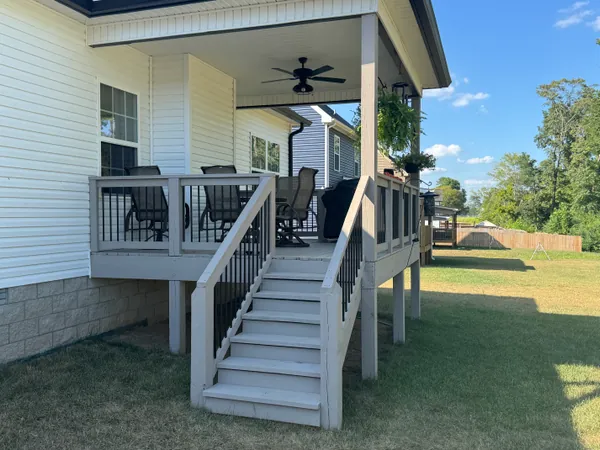 Covered back porch with a gray painted deck, a run of steps down to the lawn, and a white rail with black metal balusters running along the porch and down both sides of the steps.