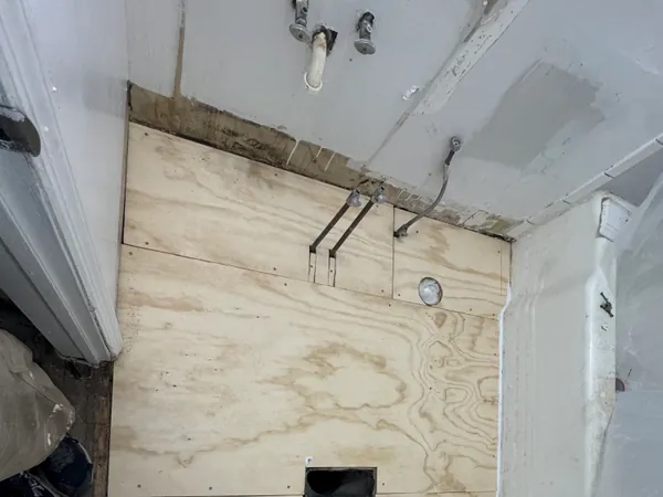 Tub alcove stripped back to the plywood backer with the wall framing and valve rough-in exposed before the surround goes back.
