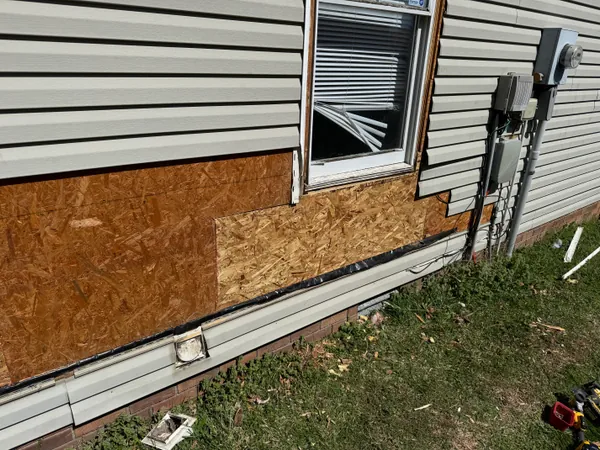 The same wall rebuilt and sheeted in new OSB across two courses under and beside the window, with flashing tape run along the bottom edge and the surrounding vinyl siding still off.