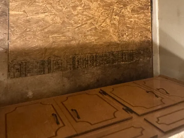 The same wall closed back up with new OSB sheathing cut tight around the shower valve escutcheon, ready for the surround to go back on, with the cabinets below untouched.